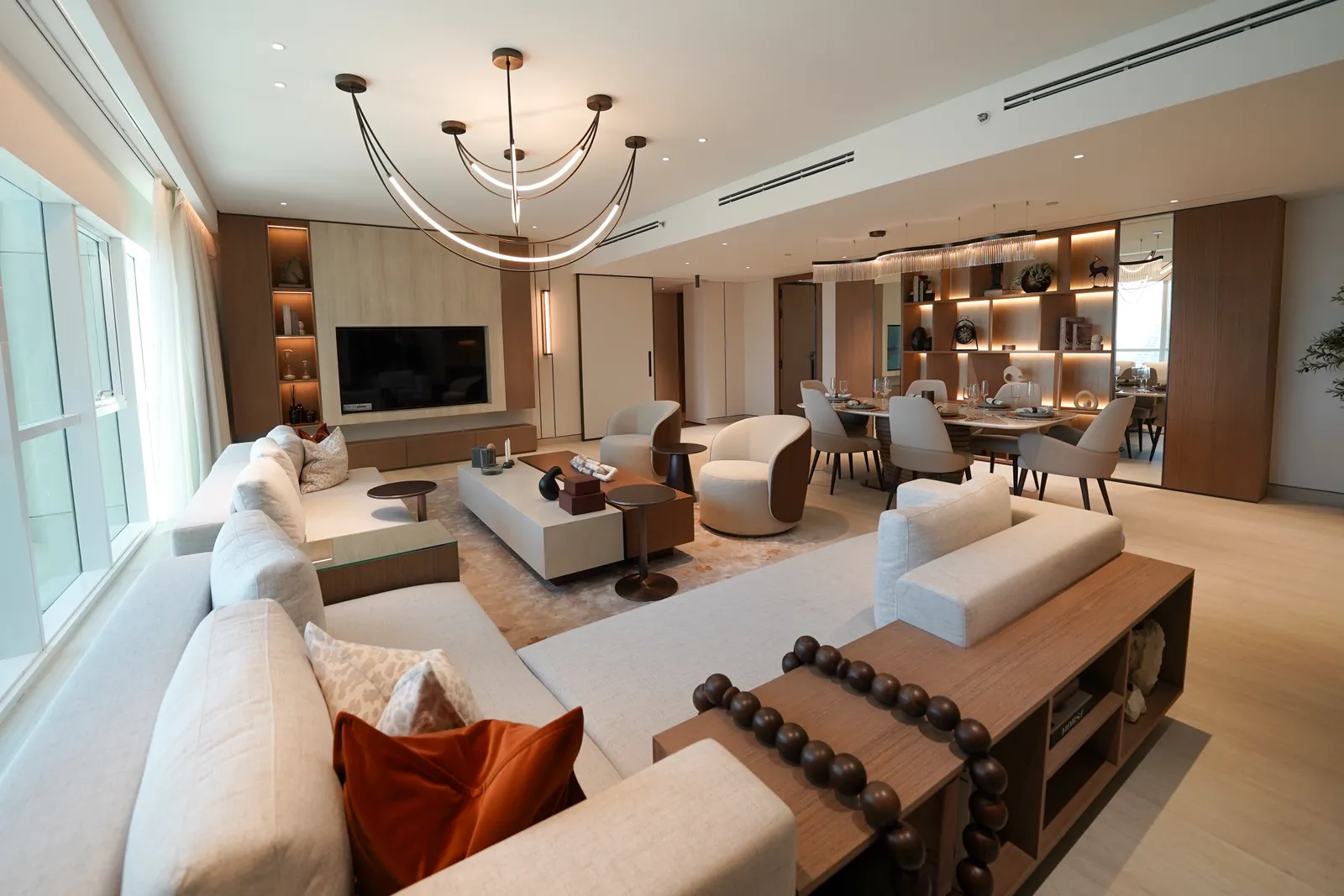 The living room from the sofa: a long cream sectional with an orange cushion and a bead garland on the console behind it, the television wall and dining table beyond