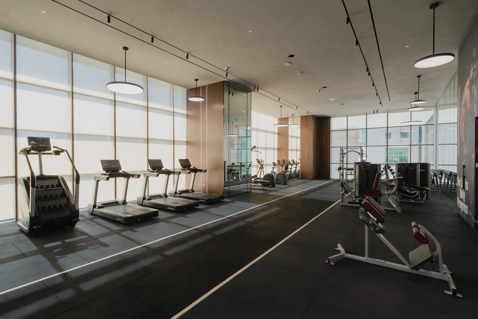 The gym along the window wall: treadmills and a stair climber, a mirrored column and strength machines beyond