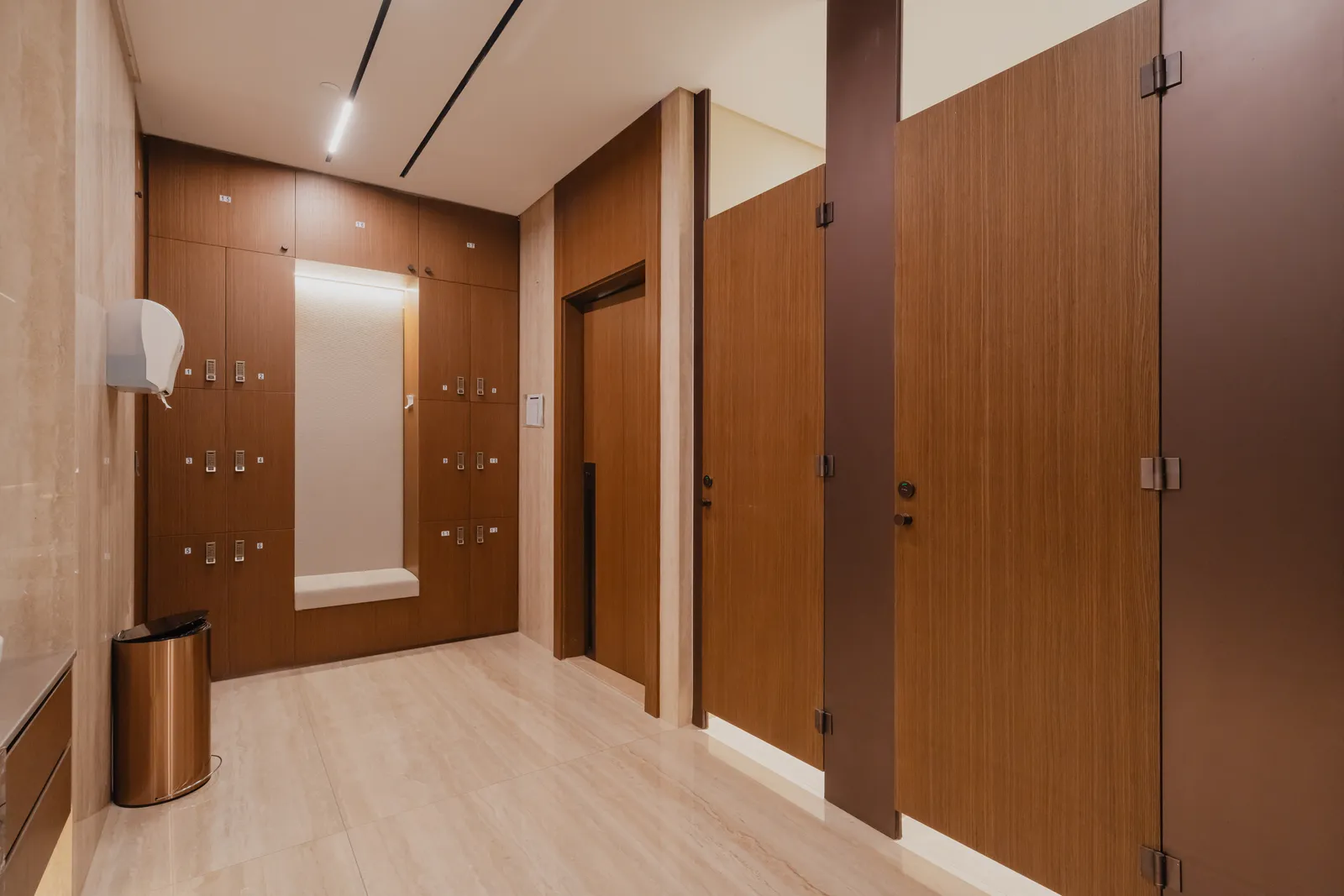 Timber lockers with a bench recess, a door and cubicle doors in a travertine-floored changing room