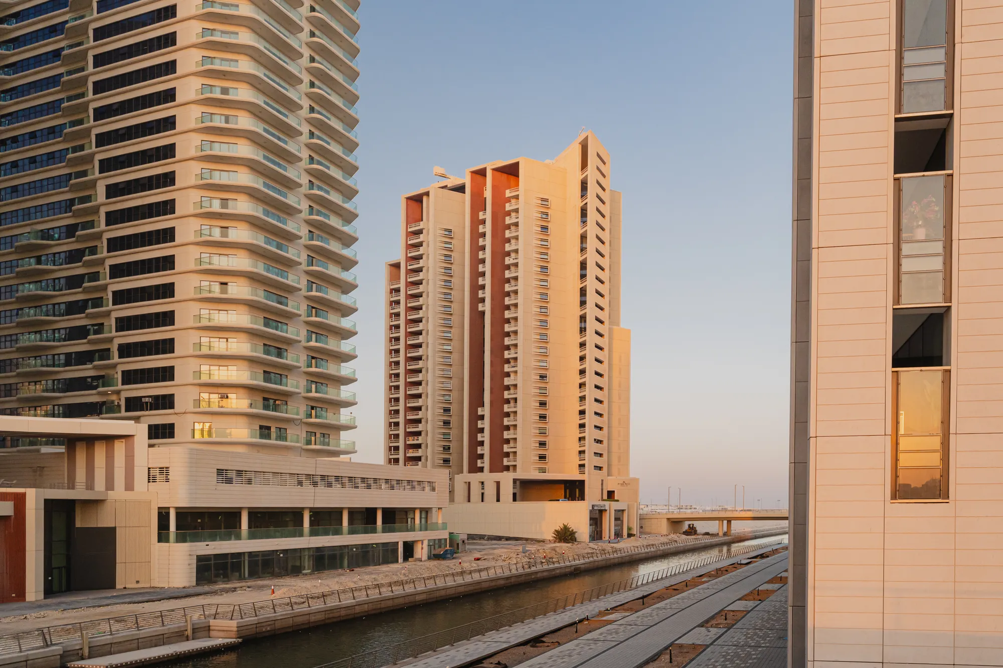 Baheen Tower at the end of a canal on Al Reem Island at sunset: the stone-clad tower with its three stepped sections, low podium buildings along the water and a neighbouring tower to the left